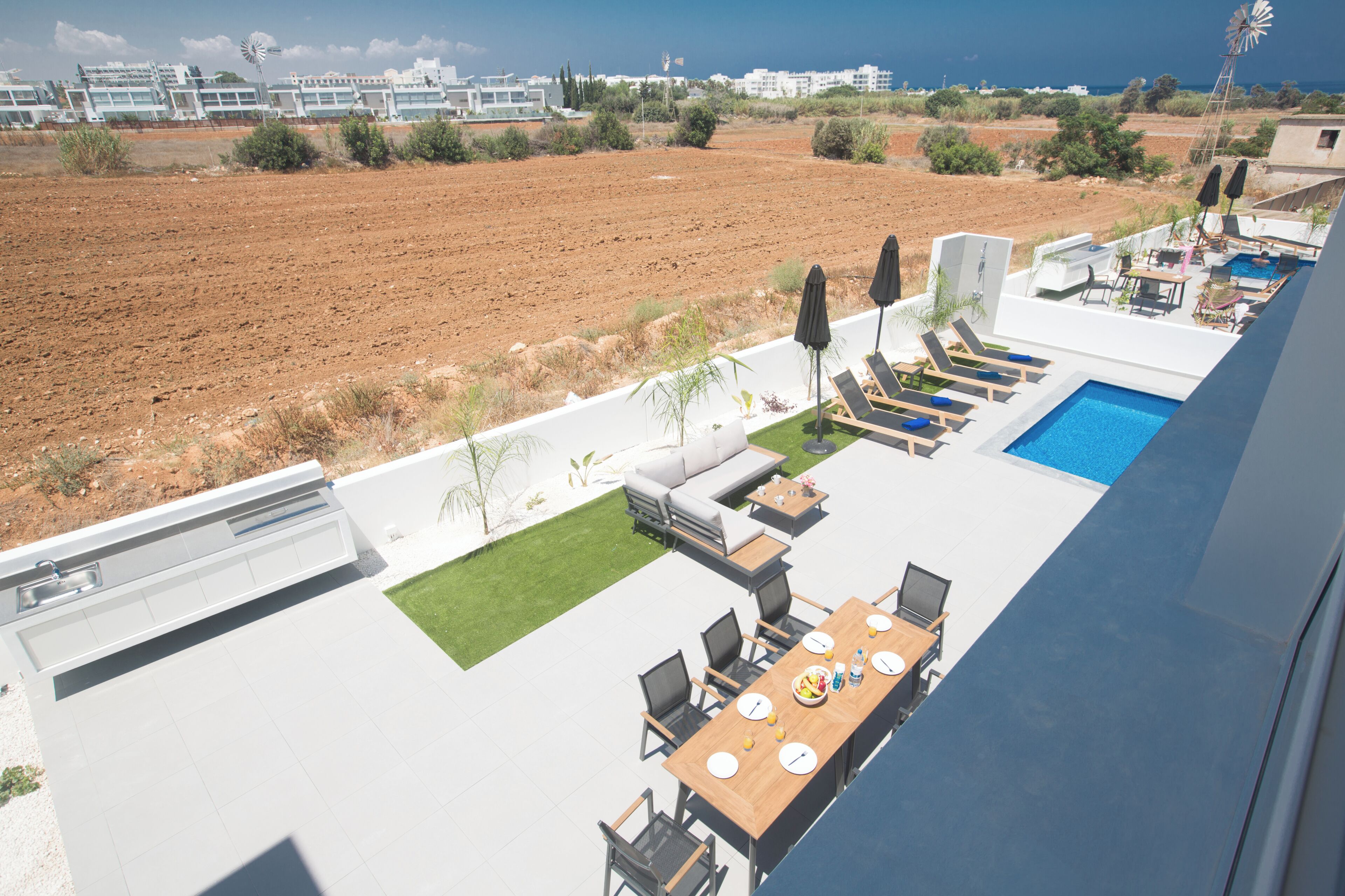 A modern outdoor dining area with a pool, lounge chairs, and a view of the surrounding landscape.