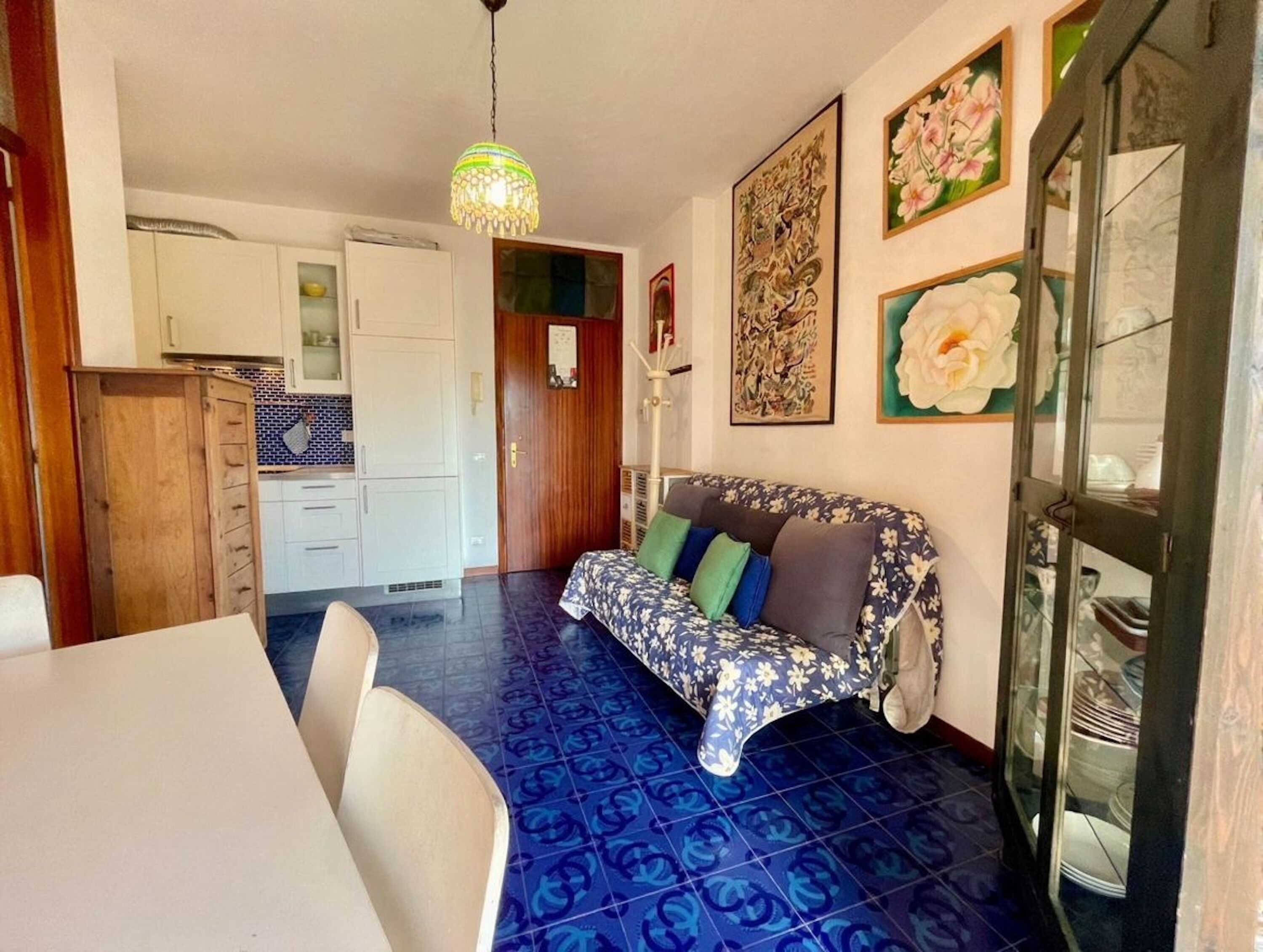 Ein Essbereich mit einem weißen Tisch und Stühlen, einer Couch mit floralem Bezug und einem blau gemusterten Boden.