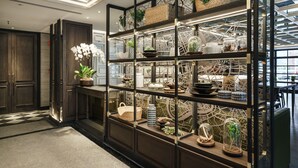 A modern interior with a wooden reception desk, glass display shelves, and a decorative map wall. - Tastoria Collection Hotel Sukhumvit (Bangkok)