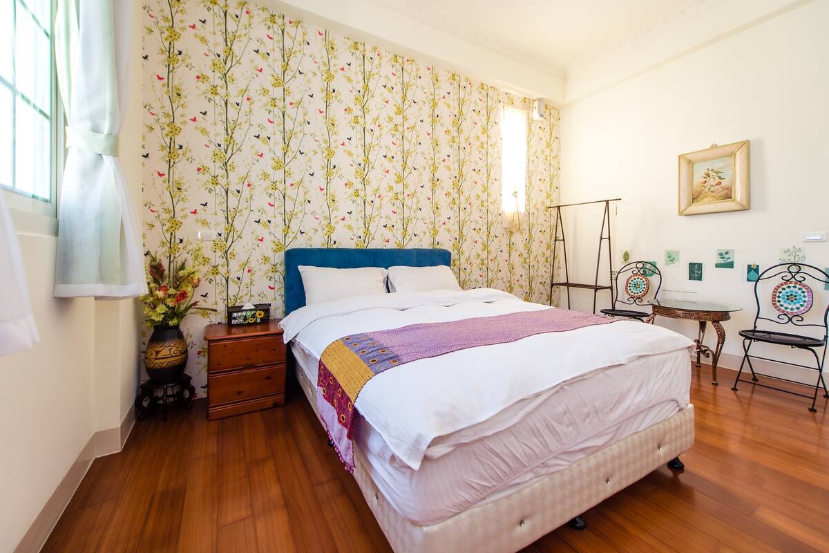 A bedroom with a bed, a nightstand, a dresser, a desk, and chairs.