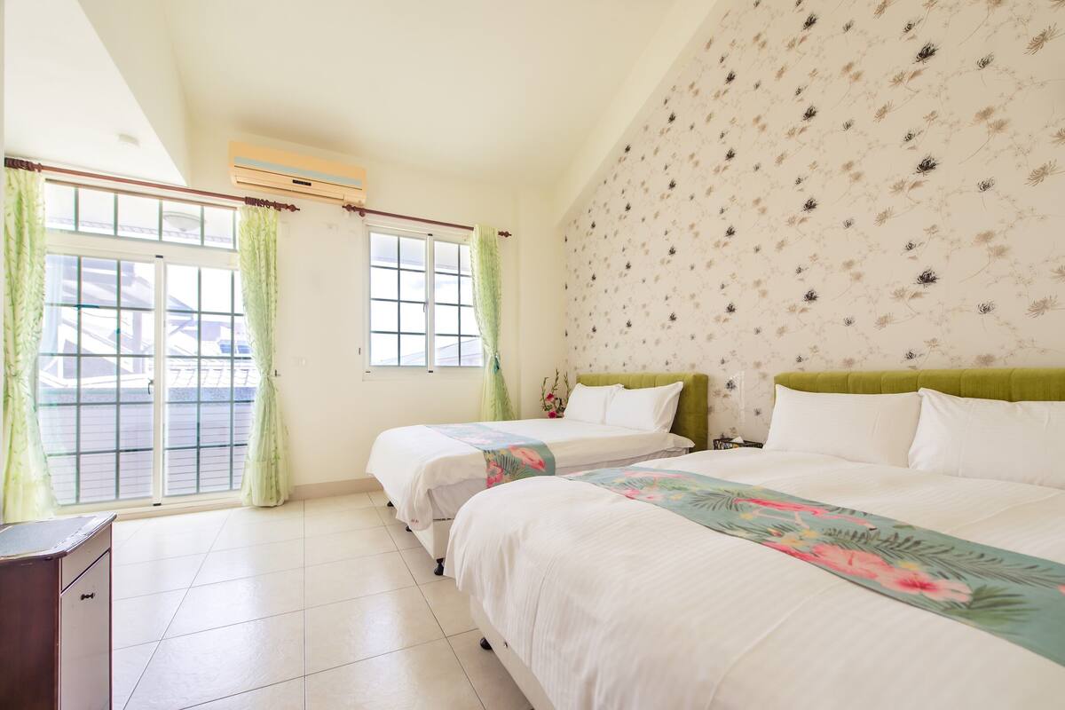 A hotel room with two beds, a window with curtains, a wall air conditioner, and a tiled floor.