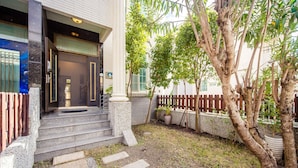 A building entrance with a set of stone steps leading up to a door, a small garden area with a tree and a wooden fence, and a paved pathway. - Ying Hsuan House (Hualien City)