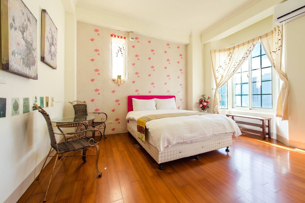 A bedroom with a bed, a chair, a table, and a window.