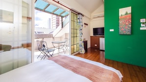 A hotel room with a bed, a green wall, a painting, a TV, and a balcony with a table and chairs. - Ying Hsuan House (Hualien City)