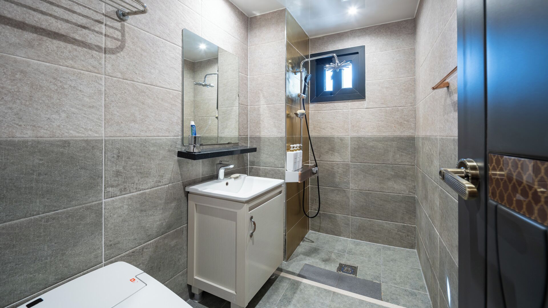 Un baño moderno con lavamanos, espejo, ducha e inodoro.