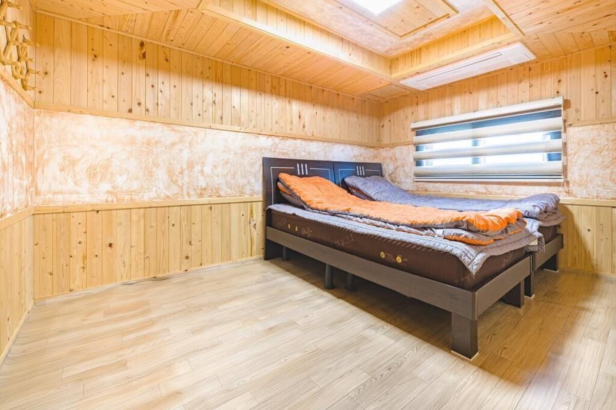 A wooden-paneled room with a bed, a window with blinds, and a skylight.