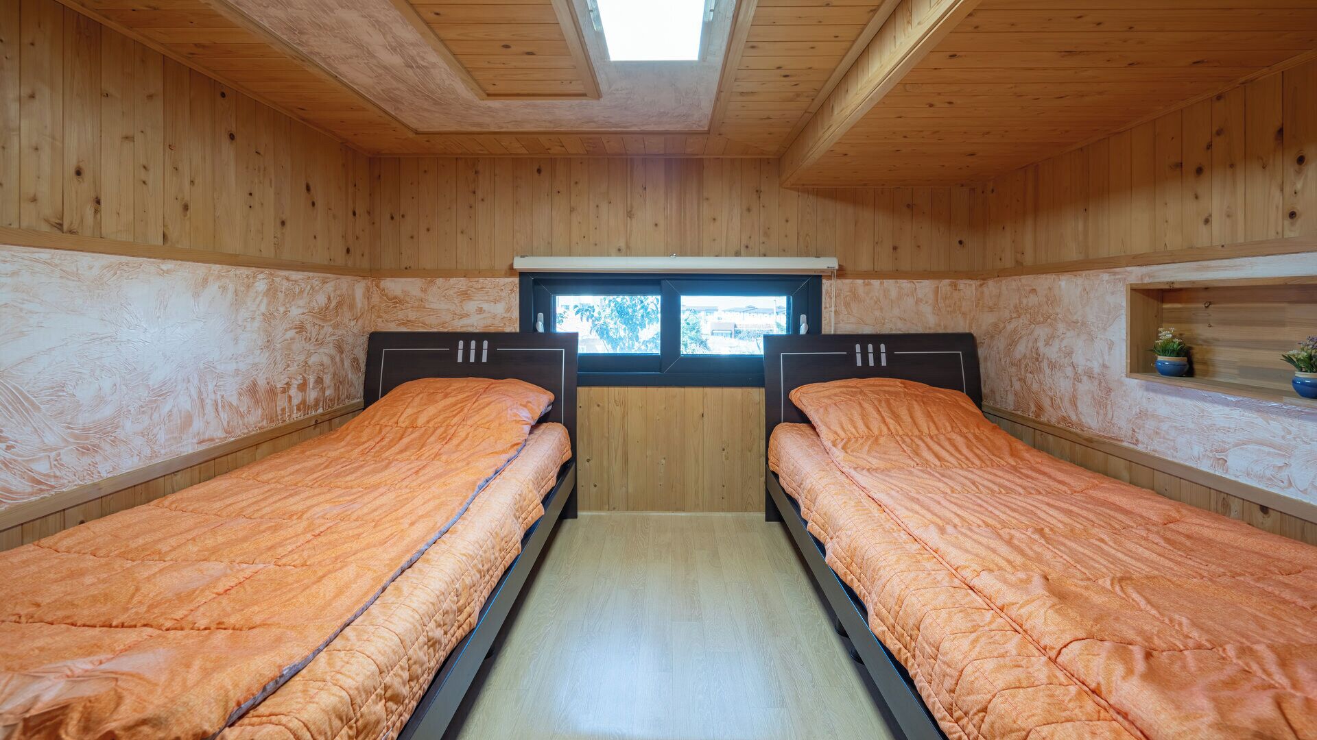 Habitación con dos camas, paredes de madera, tragaluz y ventana.