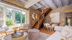 Un salón amplio con un gran ventanal, una escalera de madera y una zona de estar acogedora.