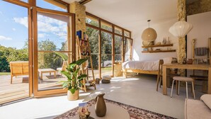 Amplia habitación con ventanas grandes, una cama, un comedor y una pequeña mesa con planta y adornos.