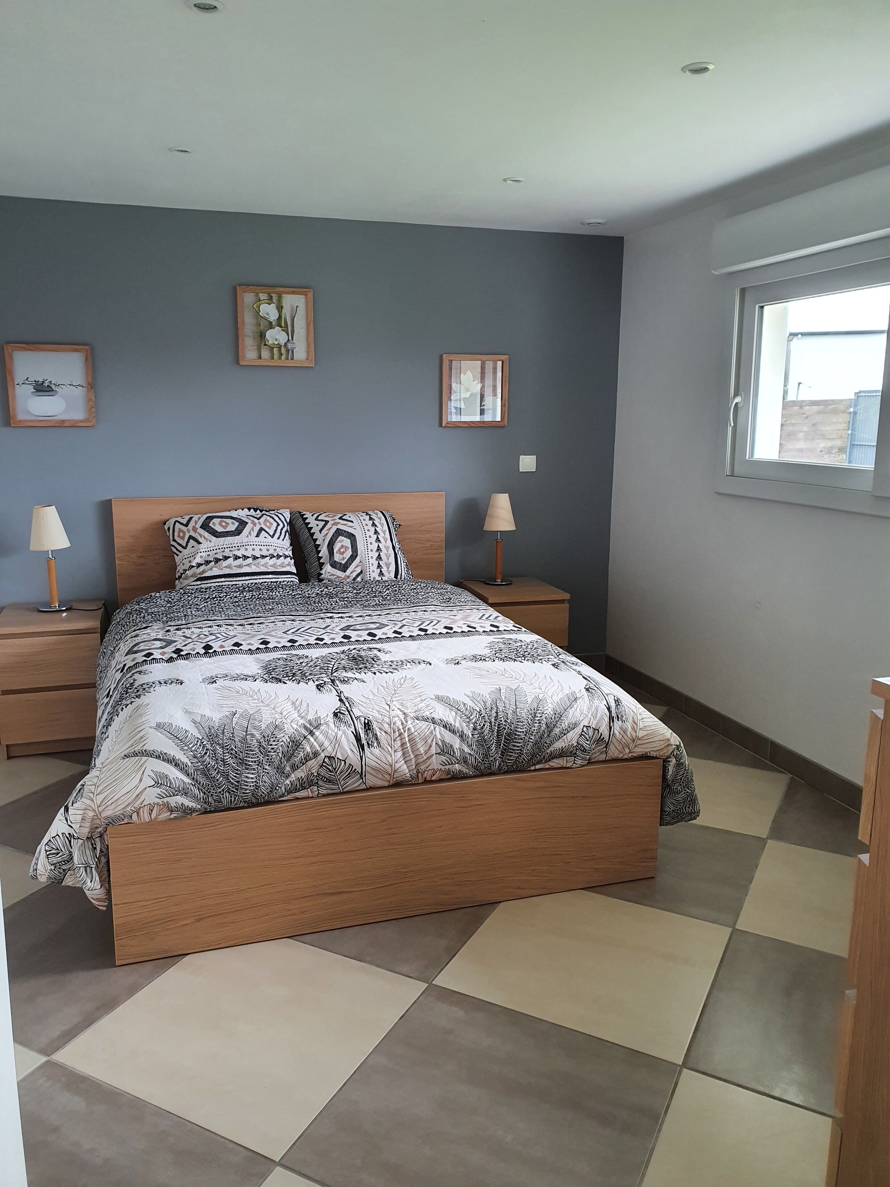 A bedroom with a bed, two bedside tables, a window, and wall art.