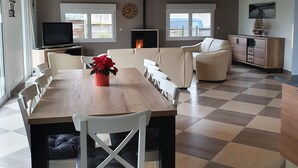 A spacious living area with a wooden dining table, white chairs, a sofa, and a television. - Charming, bright, spacious house (sleeps 12) 2 mns from the beach (Locquirec)