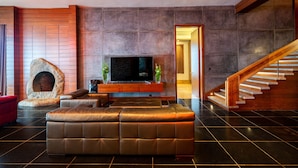 Een moderne woonkamer met een stenen open haard, een grote flatscreen televisie, een leren bank en een houten trap.