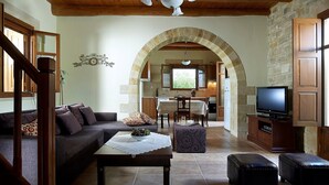 Ein gemütliches Wohnzimmer mit einer Couch, einem Couchtisch und einem Fernseher. Durch einen Bogen ist eine Küche erkennbar.