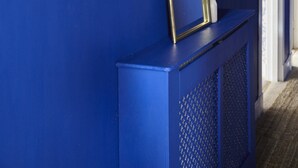 Een hal met een blauwe muur, kunstwerken en een decoratieve spiegel met pluisgras.