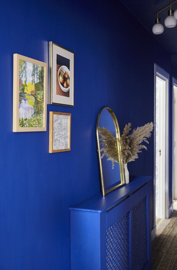 A hallway with a blue wall, framed artwork, and a decorative mirror with pampas grass.