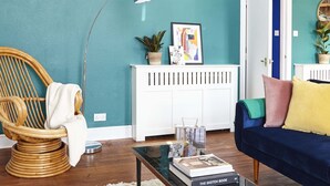 Een woonkamer met turquoise muren, een rieten stoel, een blauwe bank en een witte radiator.