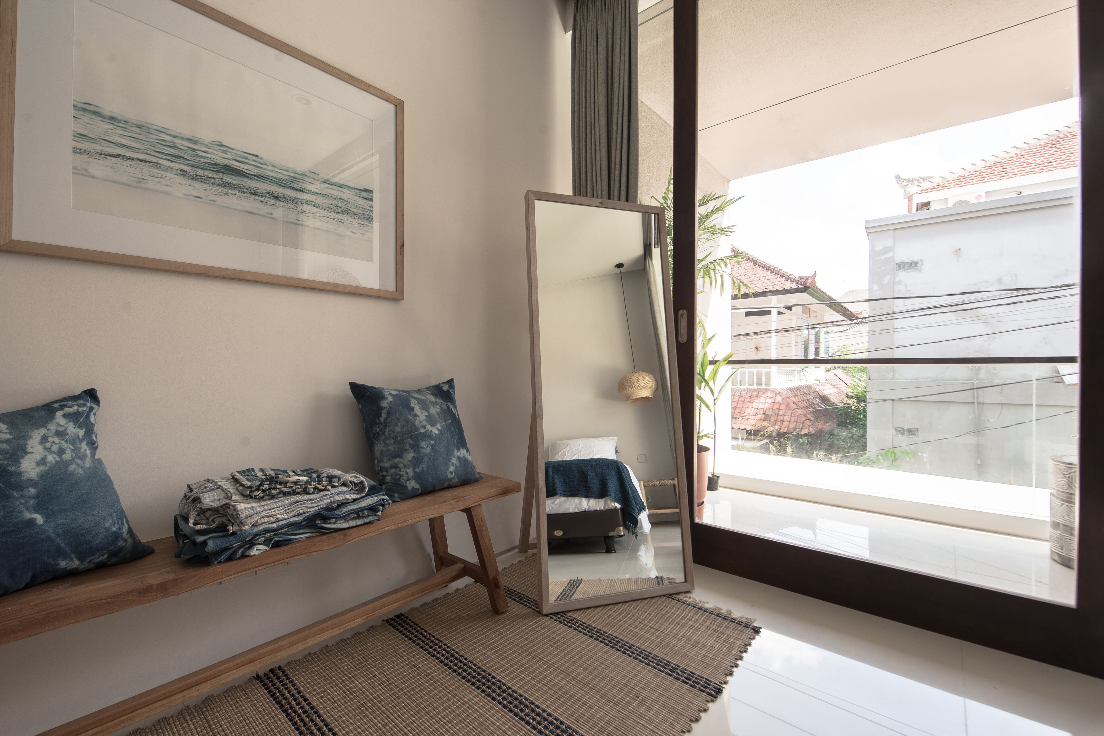 A modern bedroom with a large mirror, a bench with folded clothes, and a view of the outside.