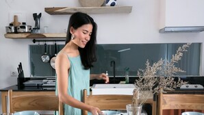 Ein Essbereich mit einem Holztisch, gedeckt für vier Personen, einer Vase mit getrockneten Blumen und einer Küche im Hintergrund.