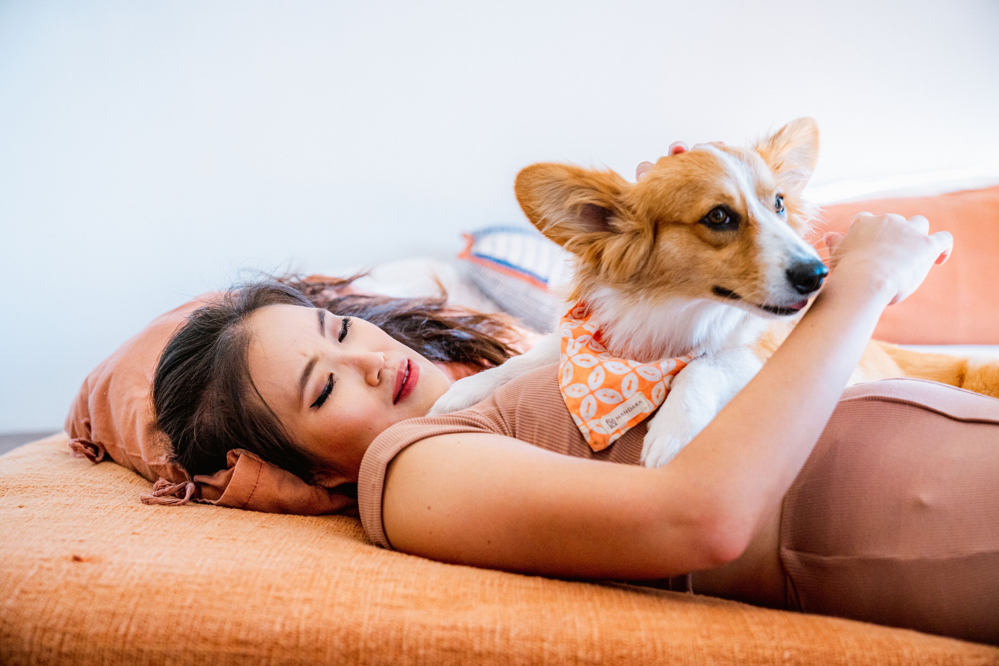A person lying on a bed with a dog wearing a bandana.