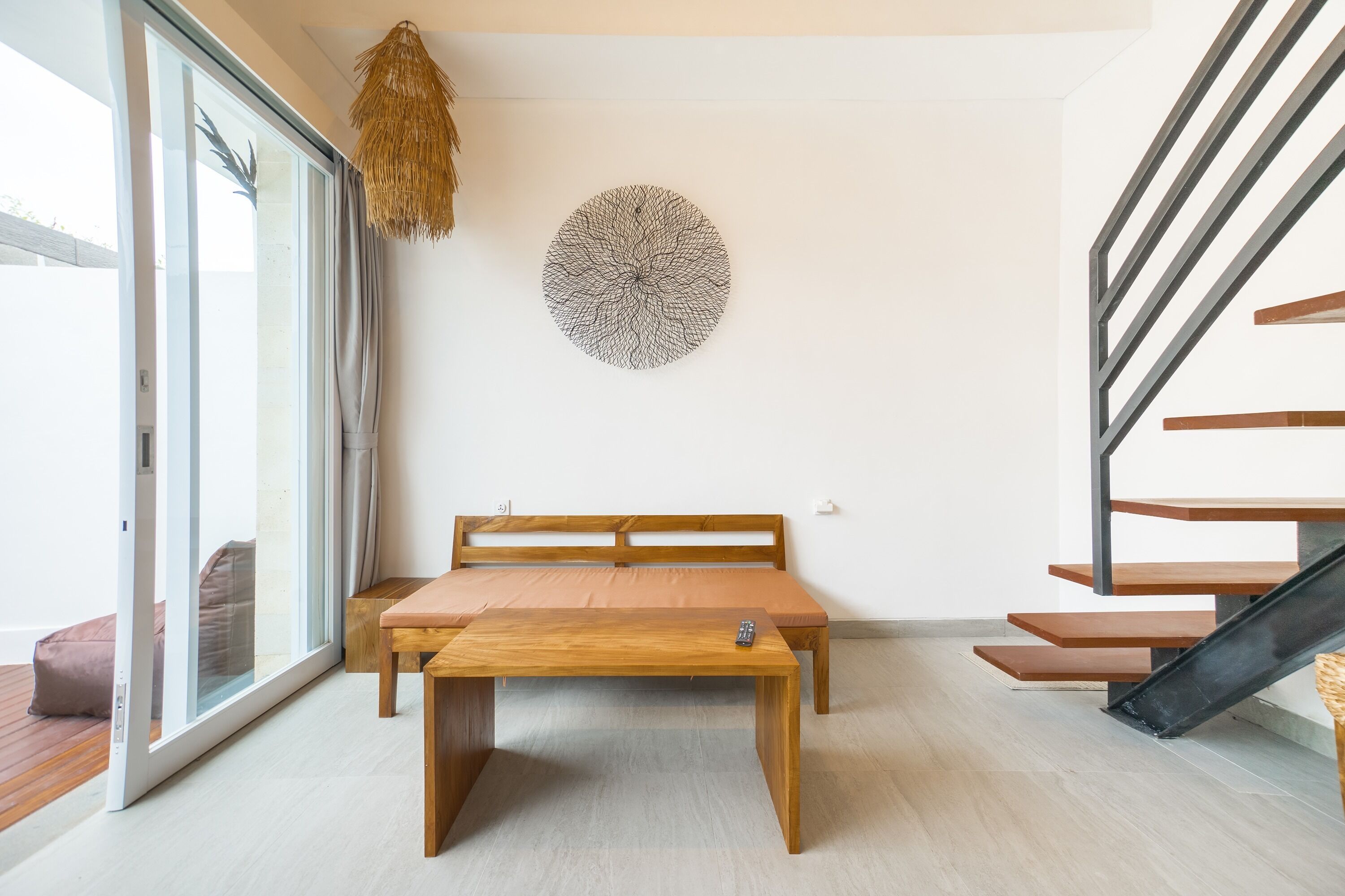 A modern living room with a wooden table, a sofa, a staircase, and a wall art piece.
