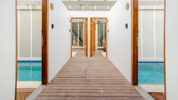 Un chemin en bois mène à un espace piscine, de part et d’autre duquel se trouvent des portes vitrées.