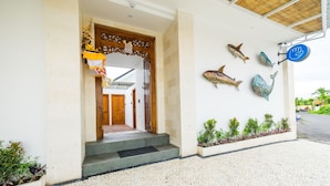 Une entrée d’immeuble avec une porte en bois, des marches menant à cette porte et des motifs décoratifs représentant des poissons sur le mur.