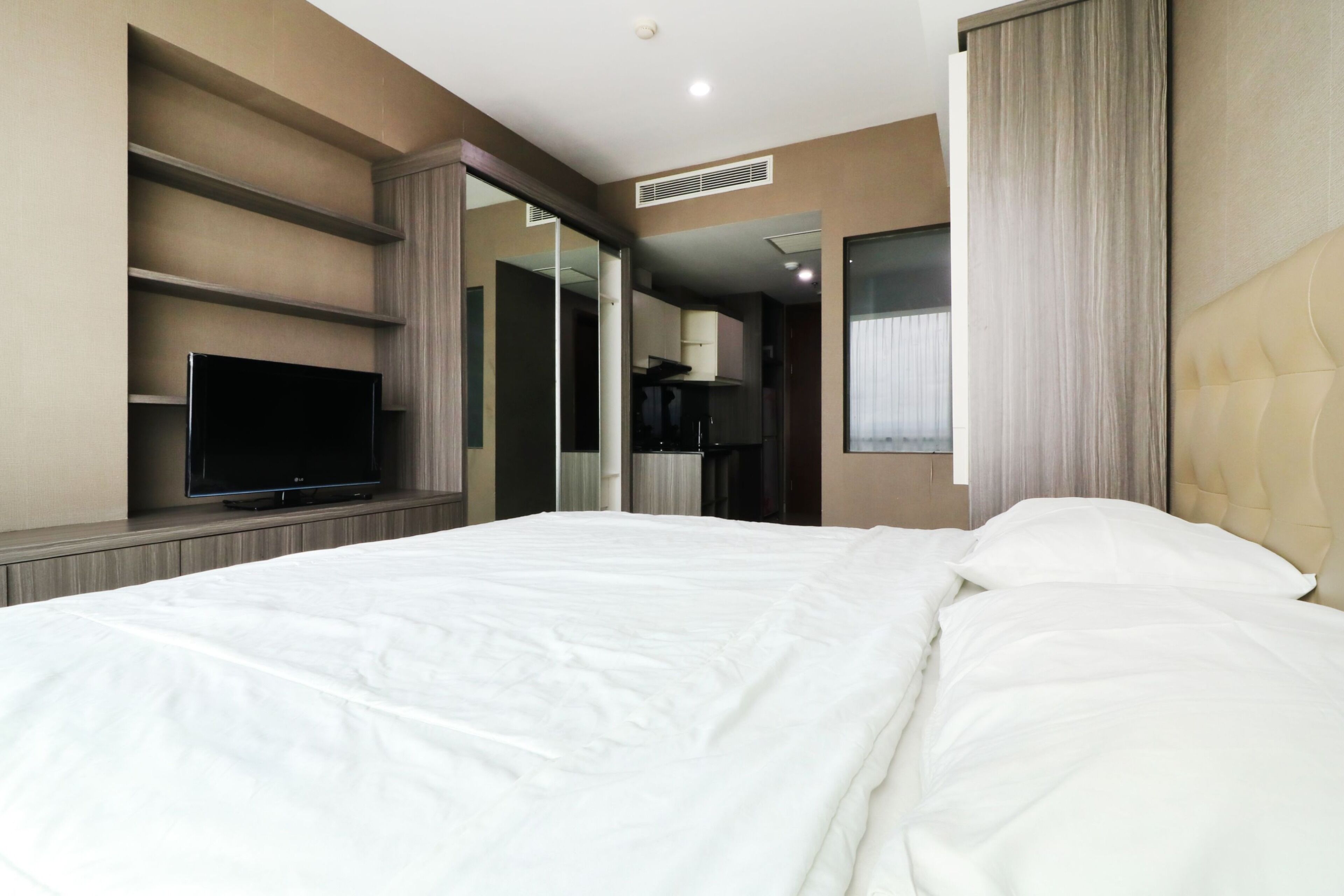 Ein modernes Hotelzimmer mit einem großen Bett, einem Flachbildfernseher, einem Kleiderschrank und einem durch eine offene Tür einsehbaren Badezimmer.