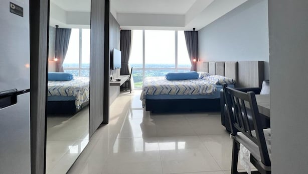 A modern hotel room with two beds, a desk, and a large window offering a city view. - U Residence 2 by Ana Room (Curug)