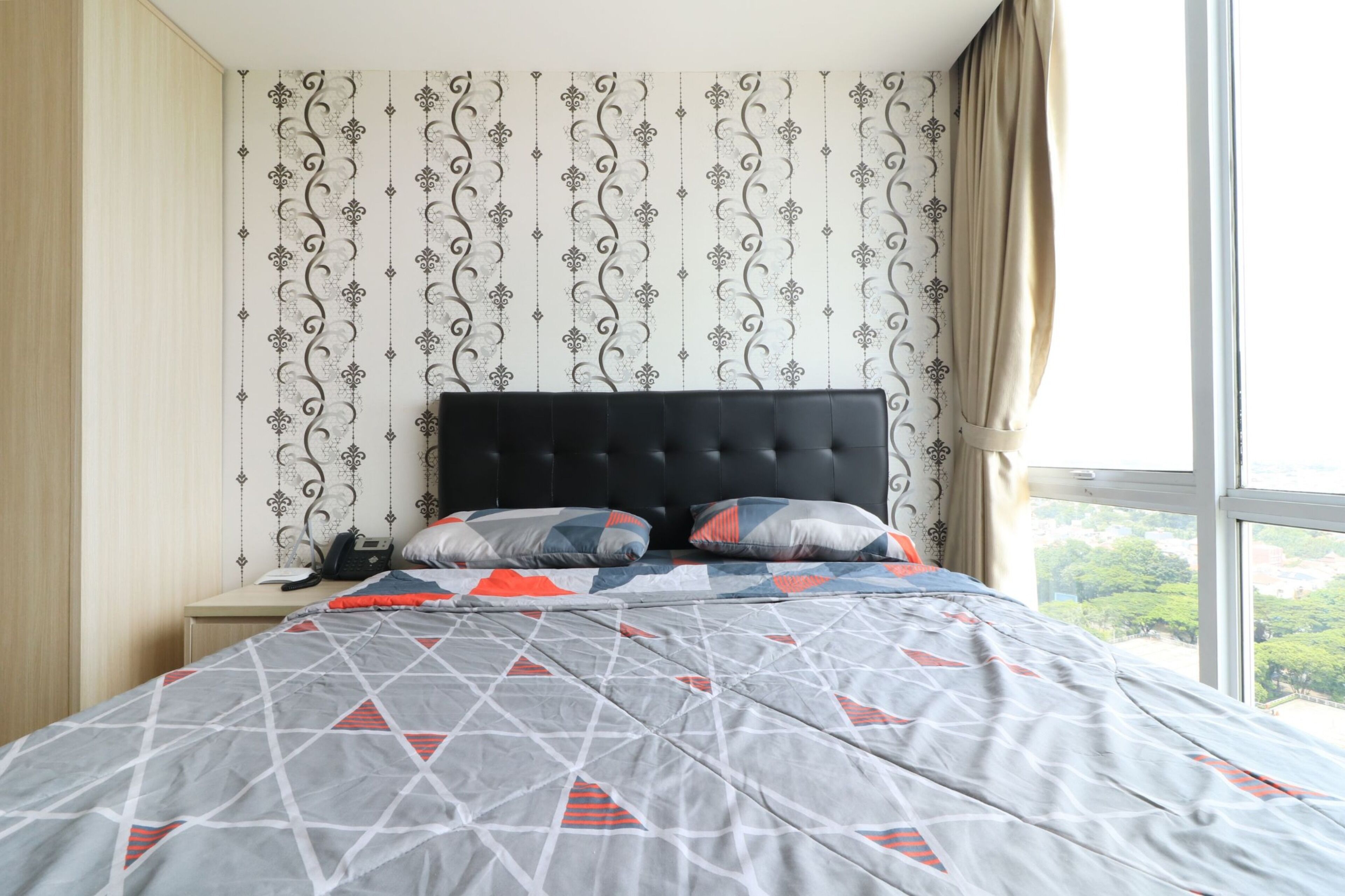 Een net opgemaakt bed met een sprei met geometrisch patroon, een zwart bekleurd hoofdbord en een nachtkastje met een telefoon.
