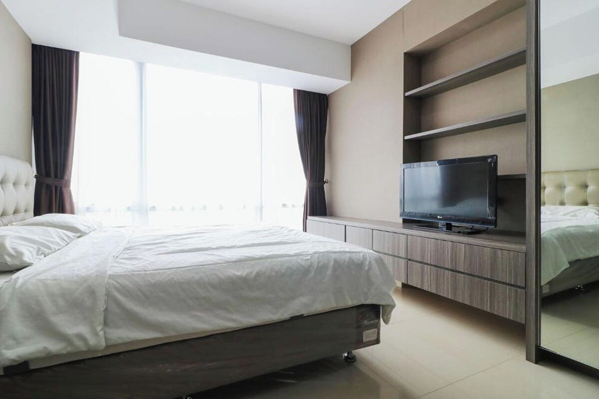Quarto moderno com uma cama grande, uma TV em uma estante de madeira e vista para a cidade pela janela.