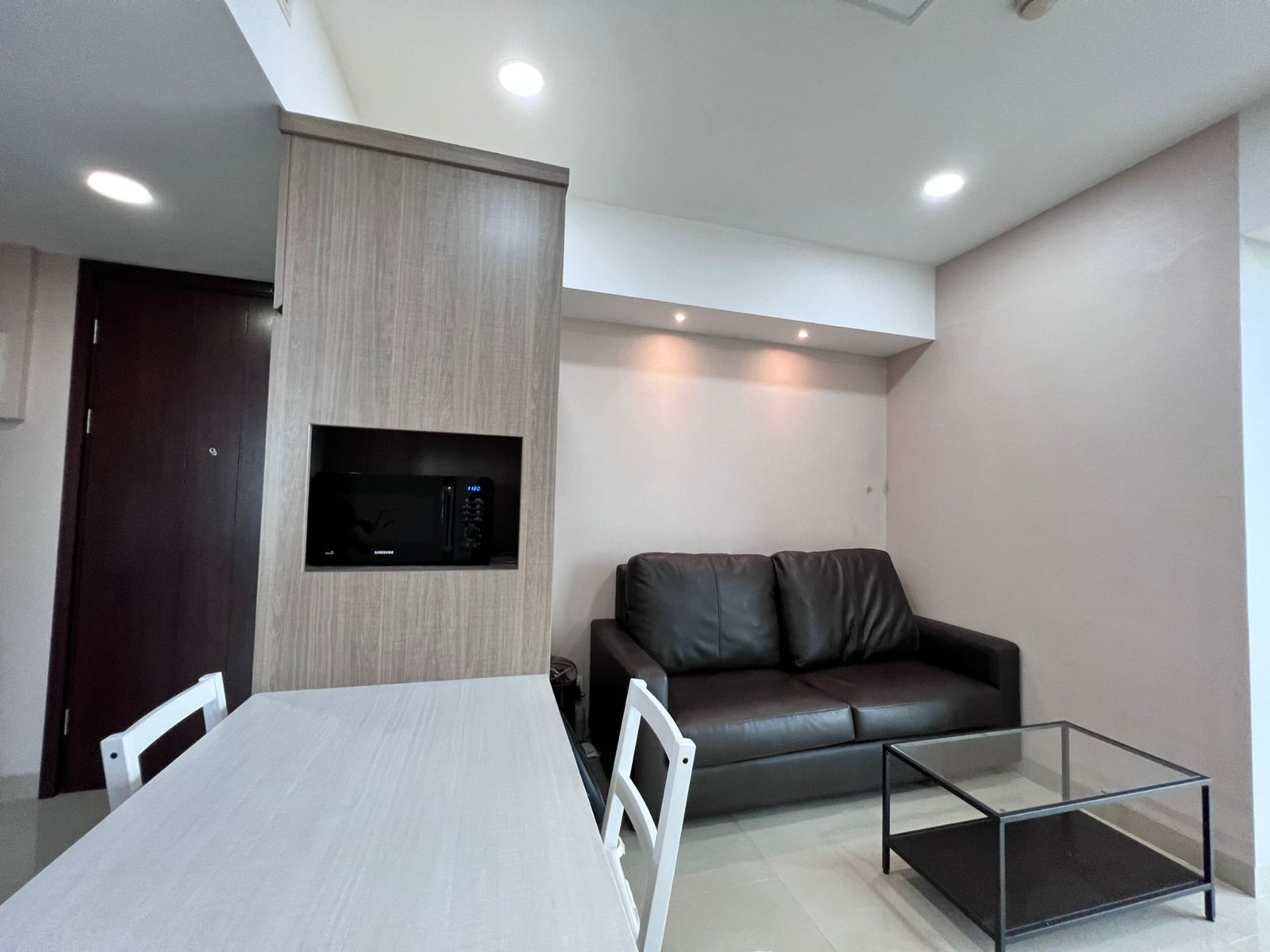 A modern living room with a dining table, a glass coffee table, a leather sofa, and a built-in microwave.