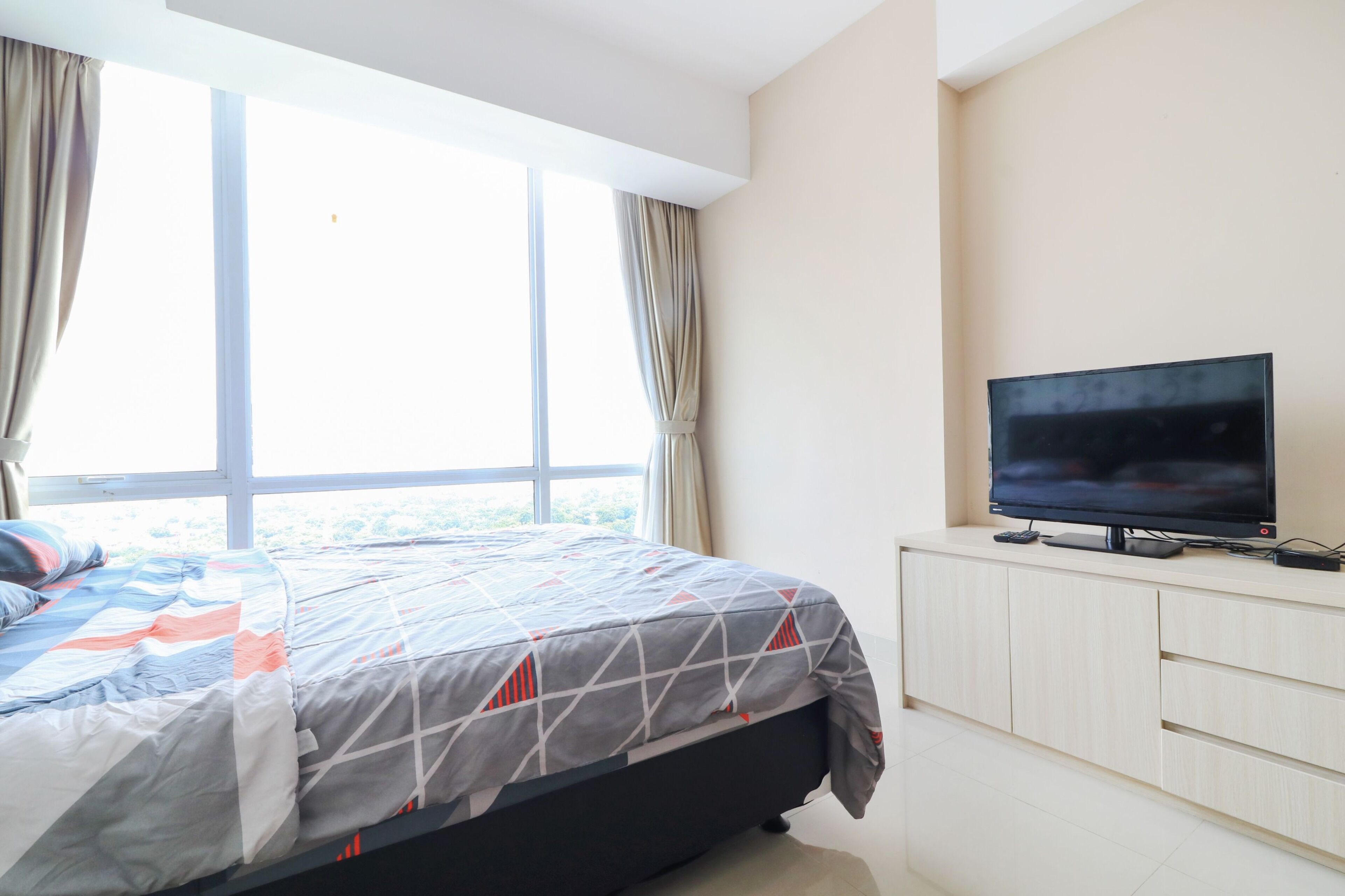 A bedroom with a bed, a TV on a stand, and a window with curtains.
