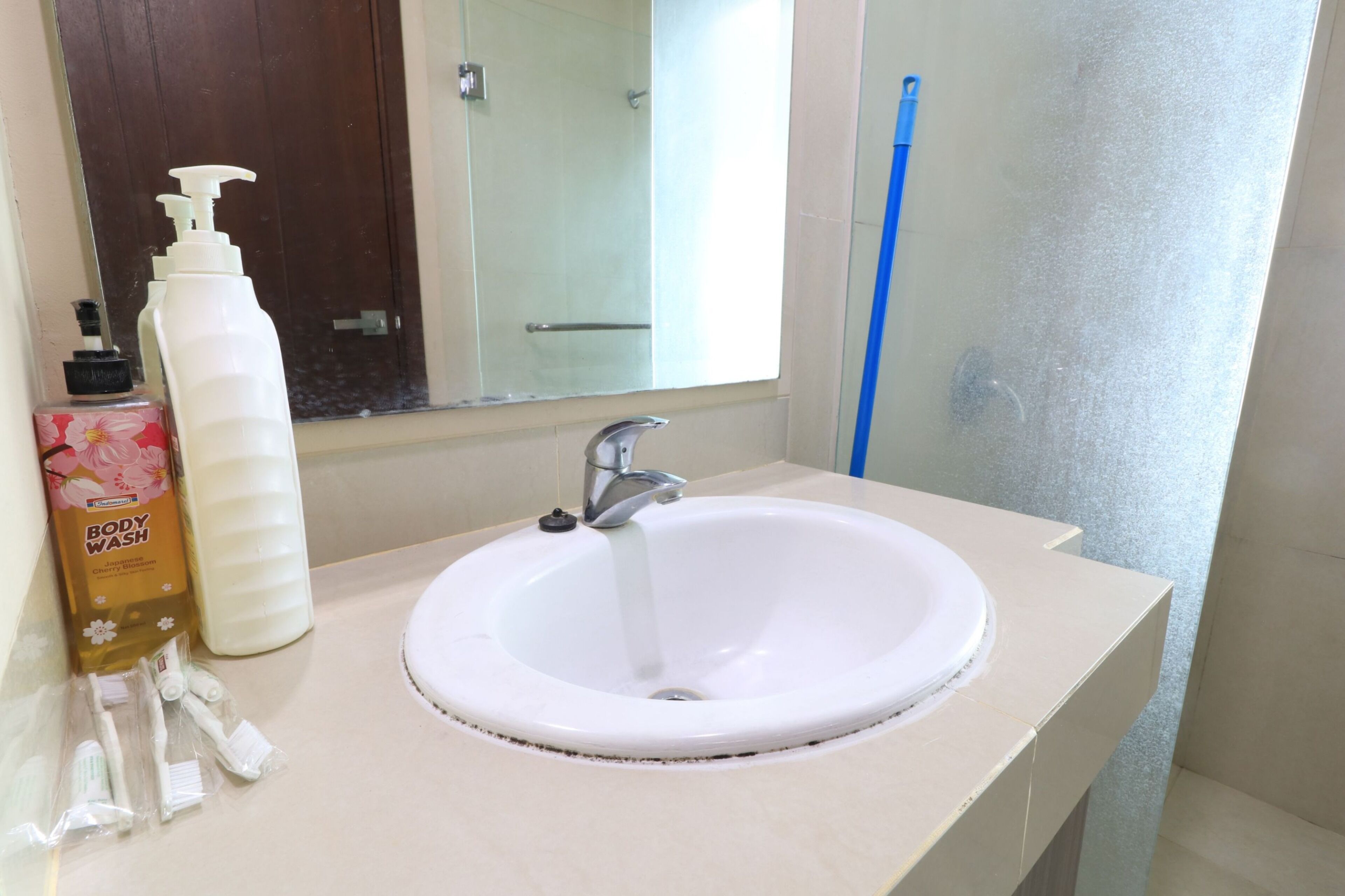 A bathroom with a white sink, a mirror, a bottle of body wash, and a blue broom.