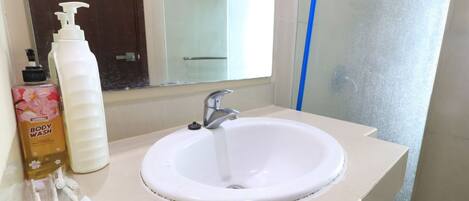 A bathroom with a white sink, a mirror, a bottle of body wash, and a blue broom.
