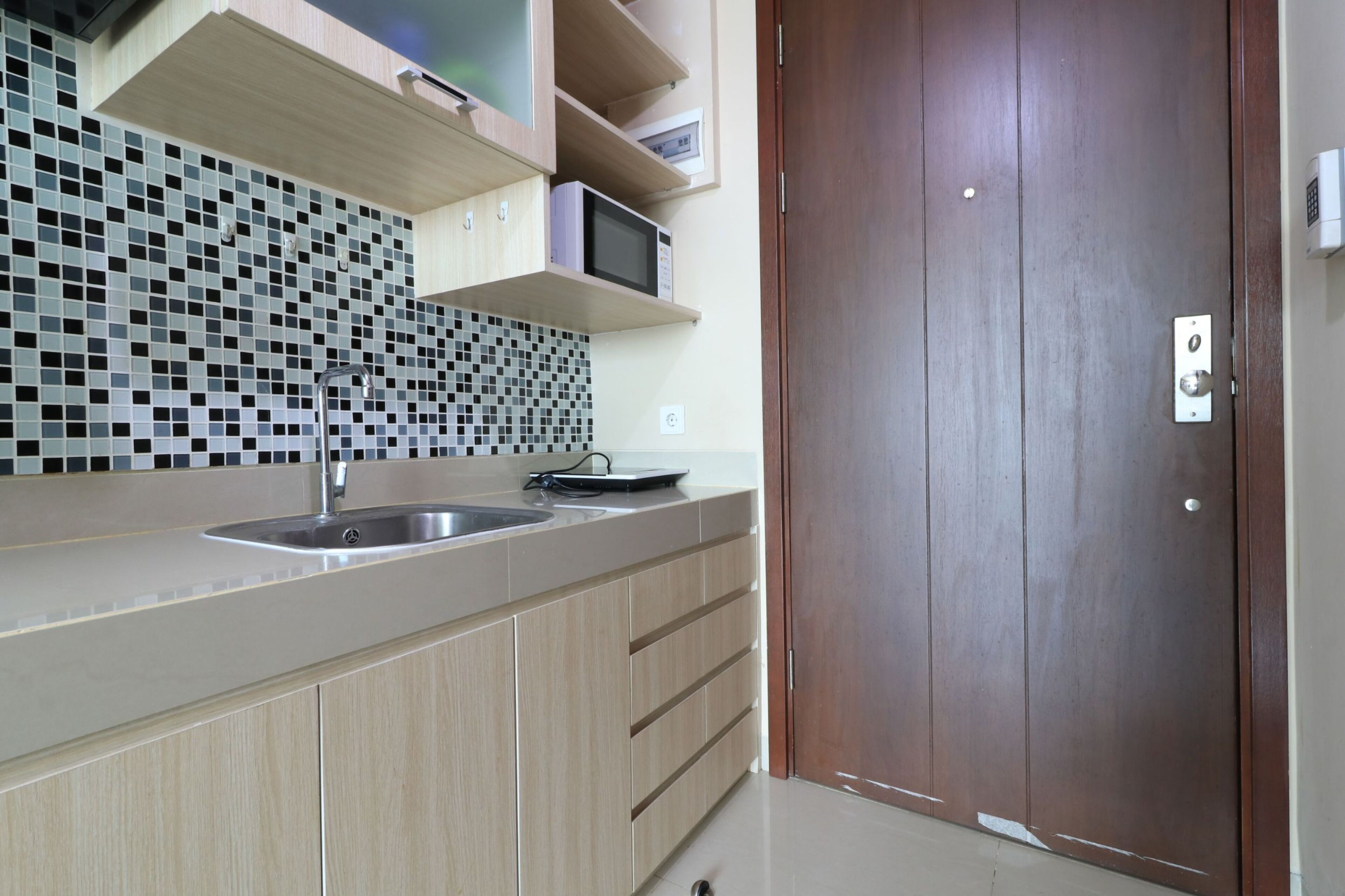 A modern kitchen with a sink, a microwave, and a wooden door.