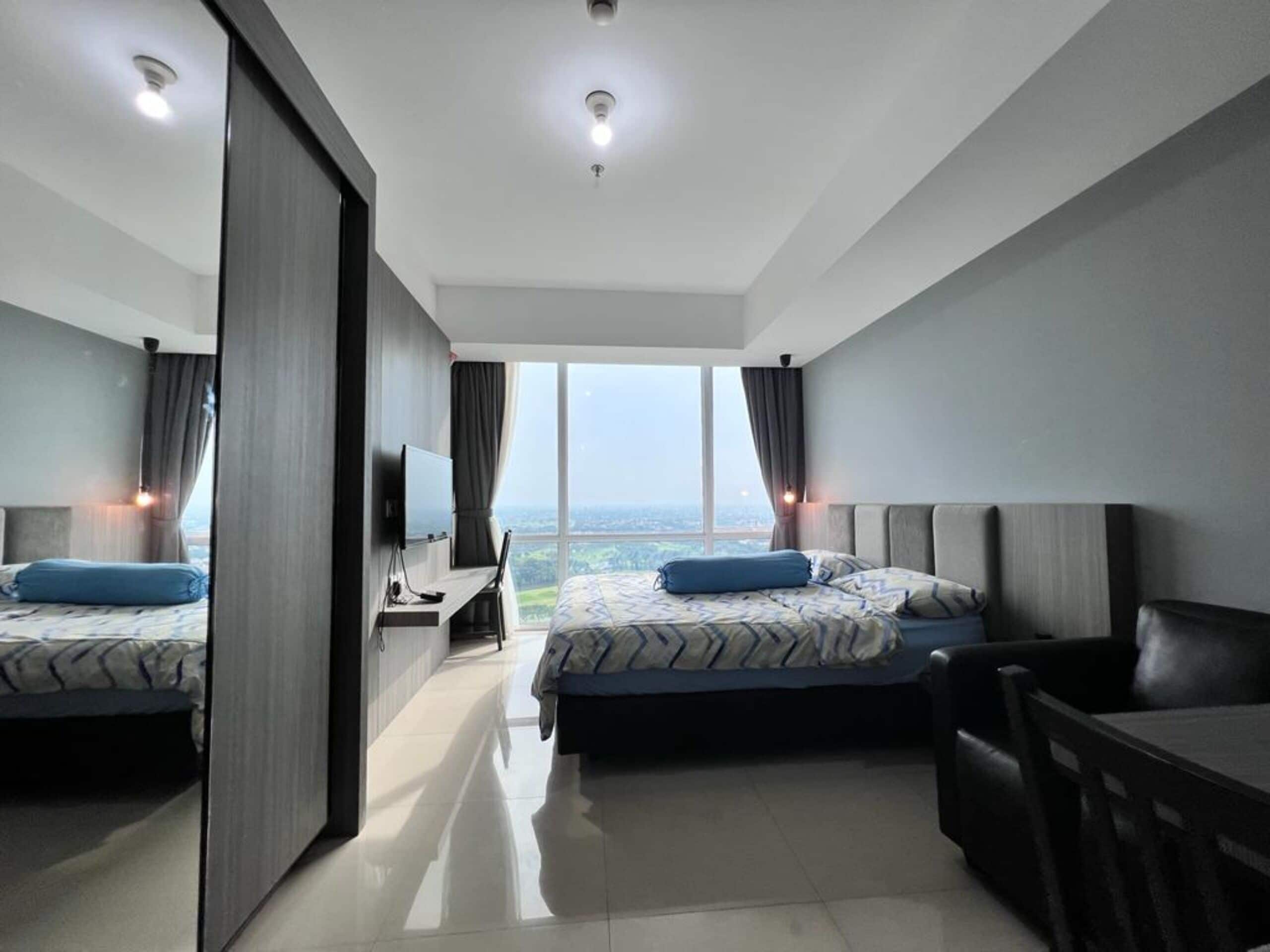 A modern hotel room with two beds, a desk, and a view of the city.