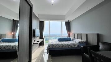 A modern hotel room with two beds, a desk, and a view of the city.