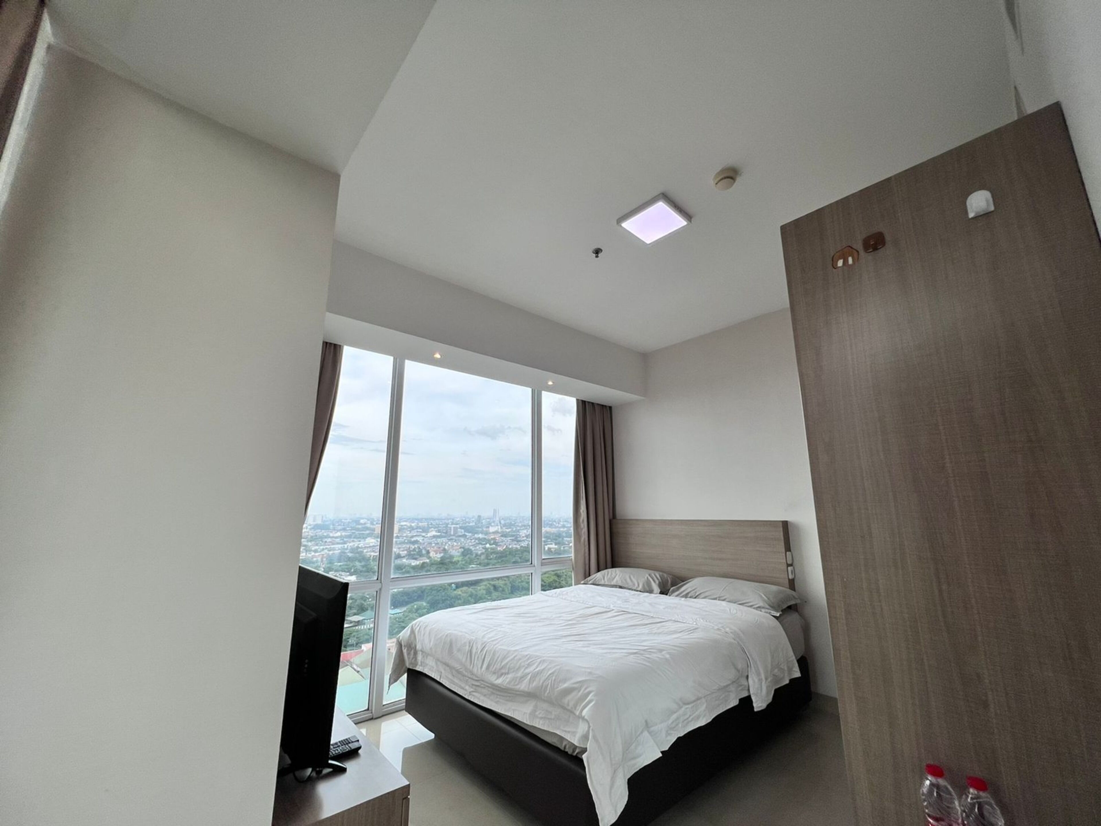 A modern hotel room with a large bed, a TV, and a city view.