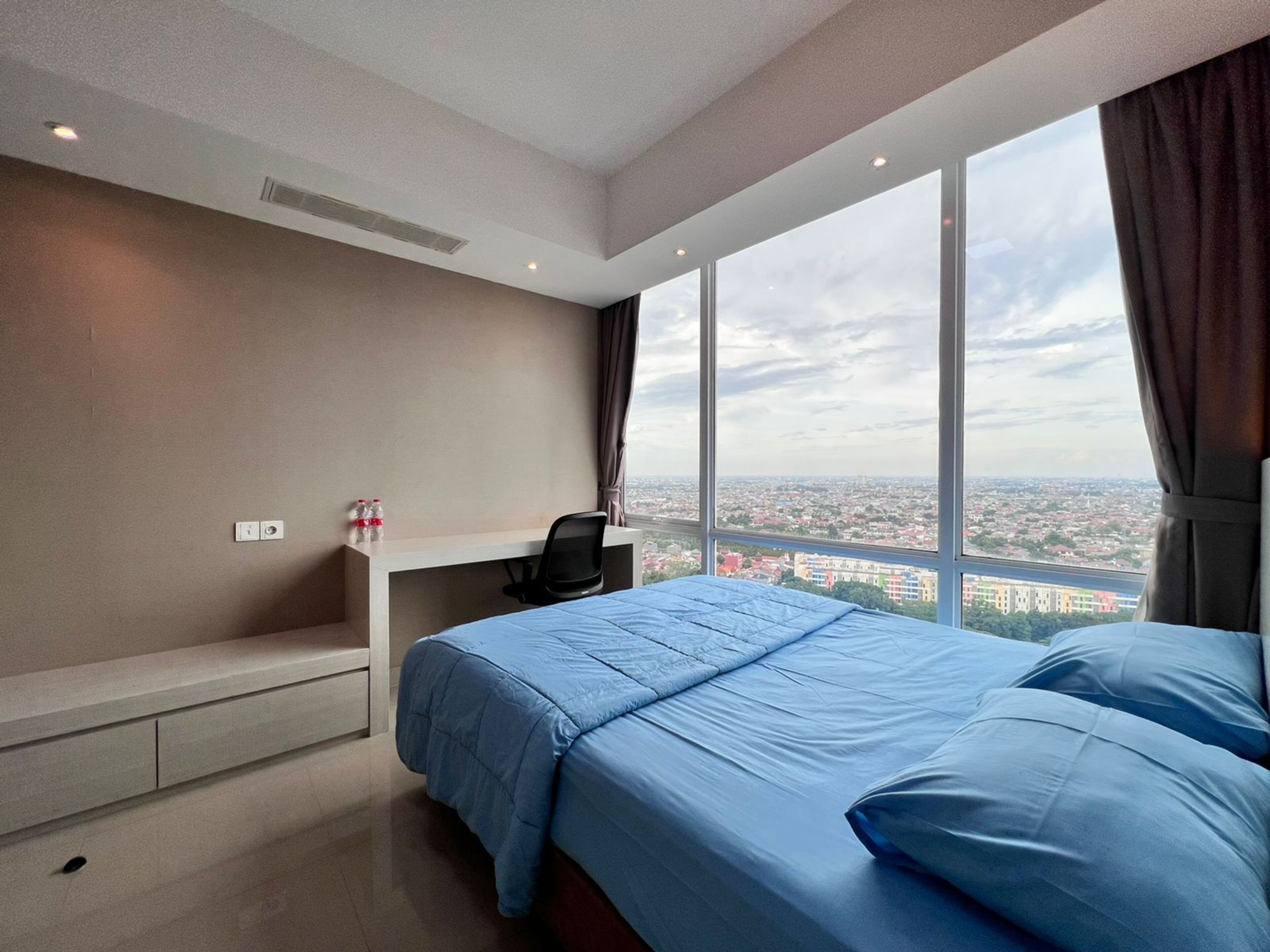 A modern hotel room with a large bed, a desk, and a view of the cityscape.