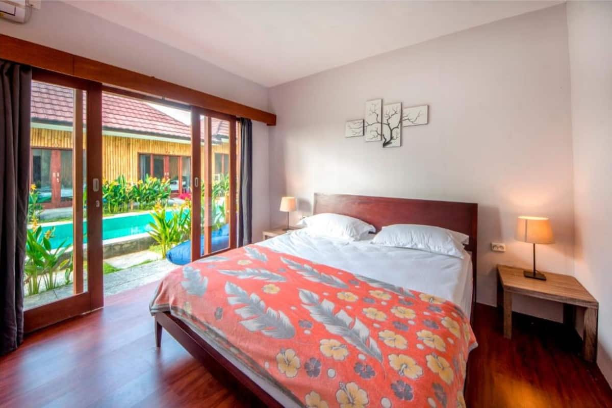 A bedroom with a bed, a nightstand, and a view of an outdoor swimming pool.