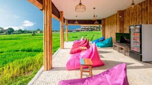 A covered outdoor seating area with bean bags, a television, and a refrigerator. - Boku Boku (Pererenan)