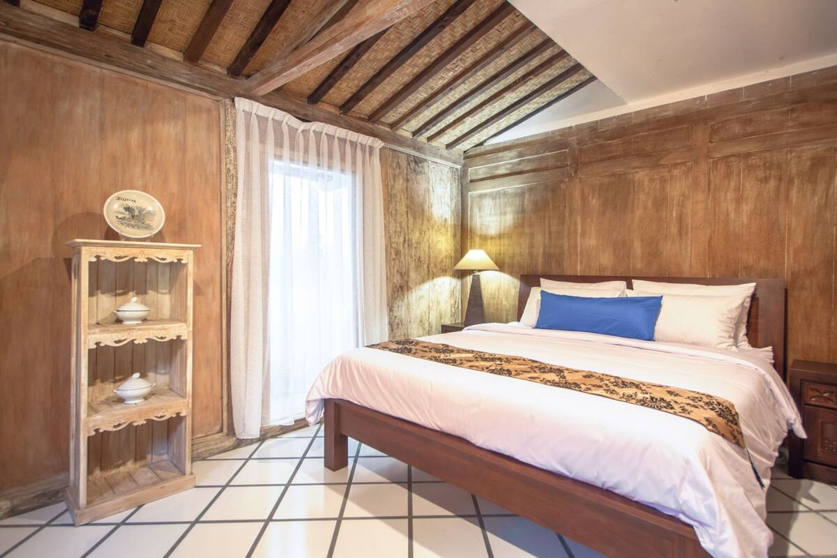 A bedroom with a wooden bed, a bedside table, a lamp, and a shelf with decorative items.