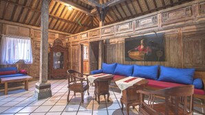 Una habitación rústica con paredes de madera y suelo de baldosas, que incluye un sofá con cojines azules, una mesa de madera con mantel blanco y un banco de madera.