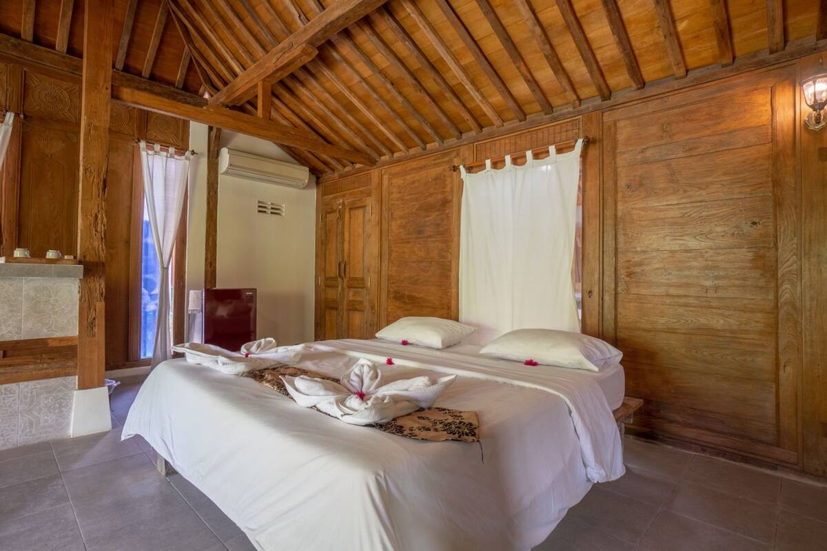 A wooden-paneled room with a large bed, a small table, and a shower area.