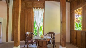 Un comedor de madera con una mesa redonda y dos sillas, una cortina blanca y vistas a zonas verdes al exterior.