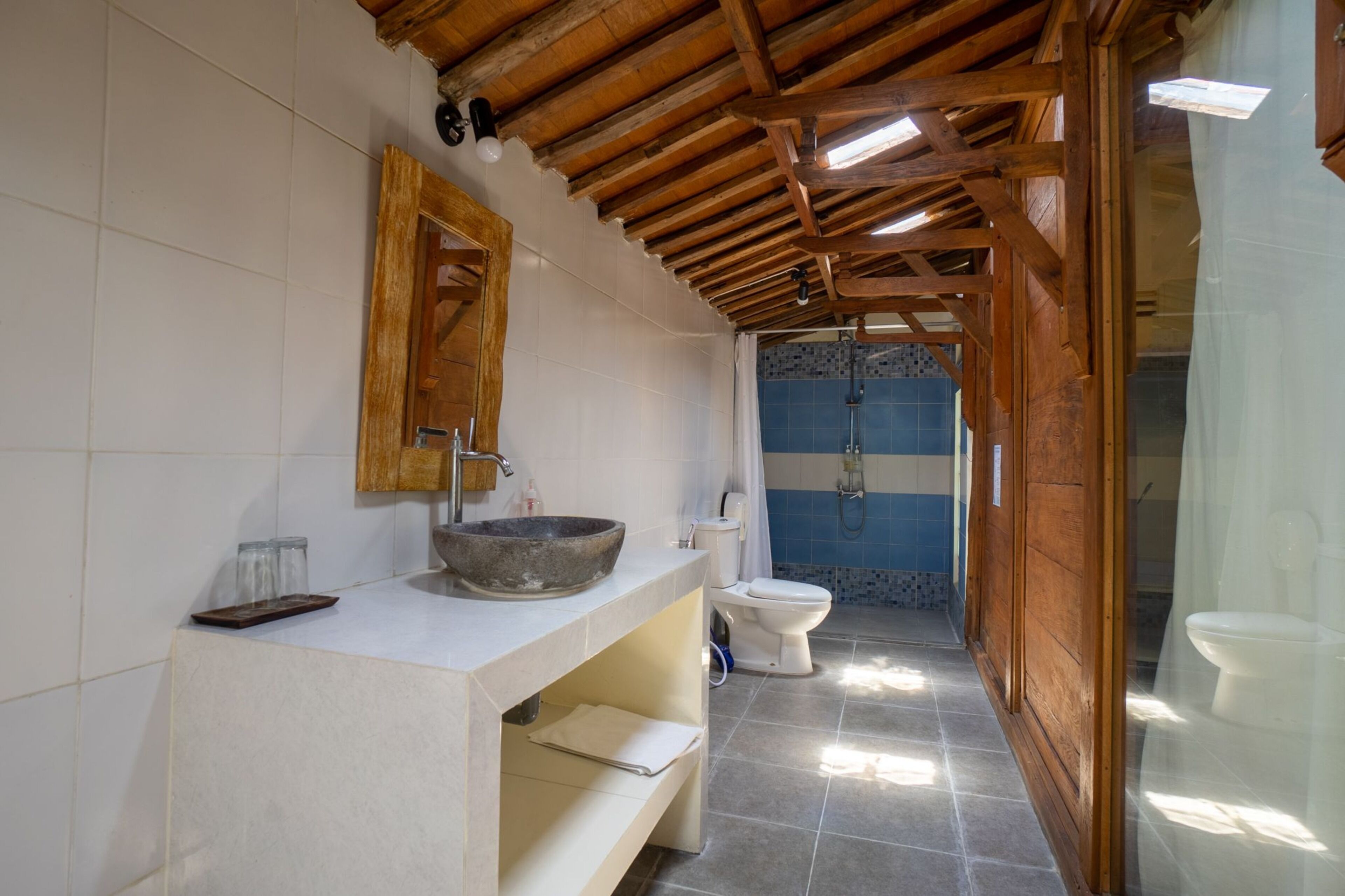 A bathroom with a wooden ceiling, a stone sink, a white toilet, and a shower area.