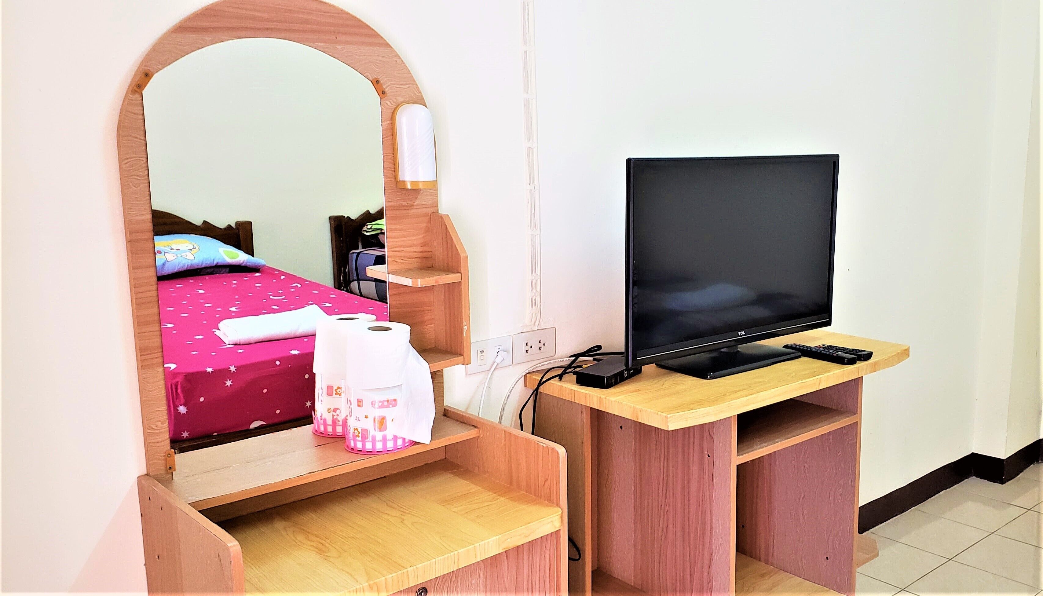 Un dormitorio con una televisión sobre un mueble de madera, una cama con edredón rosa y un espejo.