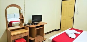 A bedroom with a bed, a wooden desk with a computer, a mirror, and a door. - Baan Yuyuen (Pathum Thani)