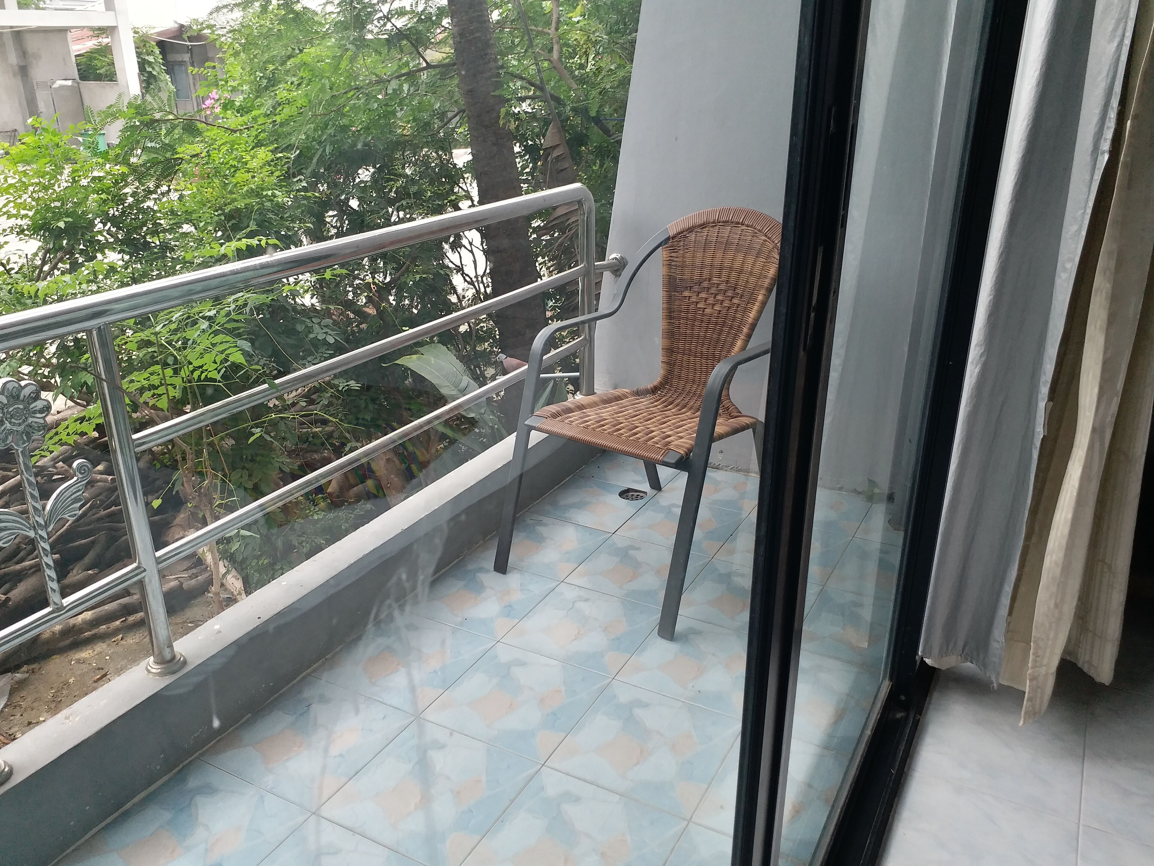 Un balcón con una silla de mimbre, barandilla de metal y suelo de baldosas.