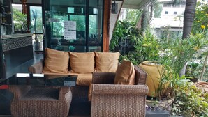 Un espace extérieur accueillant, aménagé avec des meubles en osier et une table en verre, entouré d’une végétation luxuriante et offrant une vue sur la ville.